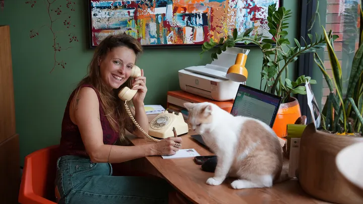 Een vrouw belt met een vintage telefoon aan haar bureau, met een kat naast haar.